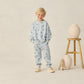 A young boy wears the Rylee & Cru Baby Boys' and Boys' Sweatshirt in light blue with small sharks print, paired with matching sweatpants, standing beside a wooden stool with two vases against a plain background.