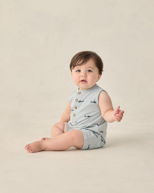 A baby wears the Rylee & Cru Baby Boys' Davis Romper—a sleeveless, light grey outfit with playful sharks print—while sitting on the floor against a neutral background.