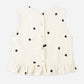 The Girls' Oceanside Top by Rylee & Cru is a sleeveless woven cotton top in white with black polka dots, featuring a button-down back and charming ruffle detail at the hem, displayed on a plain background.