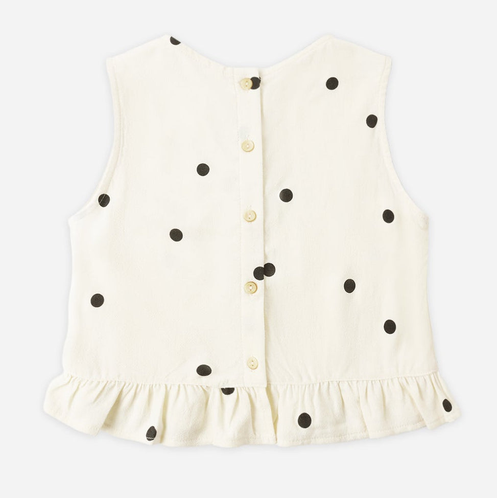 The Girls' Oceanside Top by Rylee & Cru is a sleeveless woven cotton top in white with black polka dots, featuring a button-down back and charming ruffle detail at the hem, displayed on a plain background.