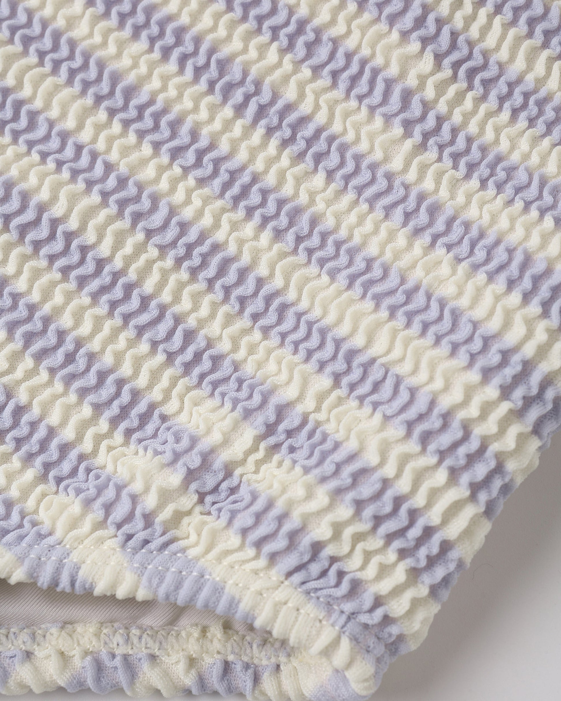 Close-up of textured fabric with alternating wavy periwinkle and off-white stripes in a ruched seersucker pattern—featured on the Rylee & Cru Moxie One-Piece UPF 50+ swimsuit for baby girls and girls.