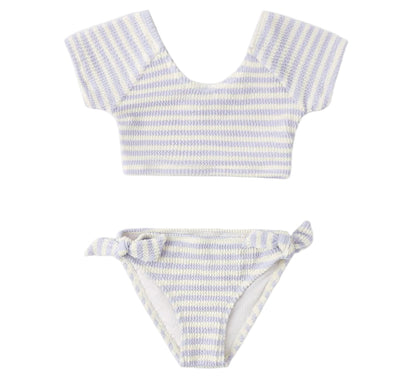 The Rylee & Cru Girls' Cropped Rashguard Set includes a short-sleeve crop top and matching bottoms with light blue and white stripes, side-tie detail, and UPF 50+ protection for stylish, sun-safe swimwear.