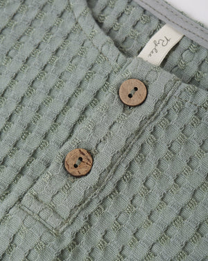 Close-up of Rylee & Cru's Baby Boys' Beau Romper in textured sea green, with two wooden buttons and a white collar tag—a stylish summer outfit.