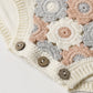 Close-up of the Rylee & Cru Baby Girls' Crochet Romper, featuring a beige, gray, and peach floral crochet pattern, three wooden buttons, and ribbed trim for a vintage-inspired look.