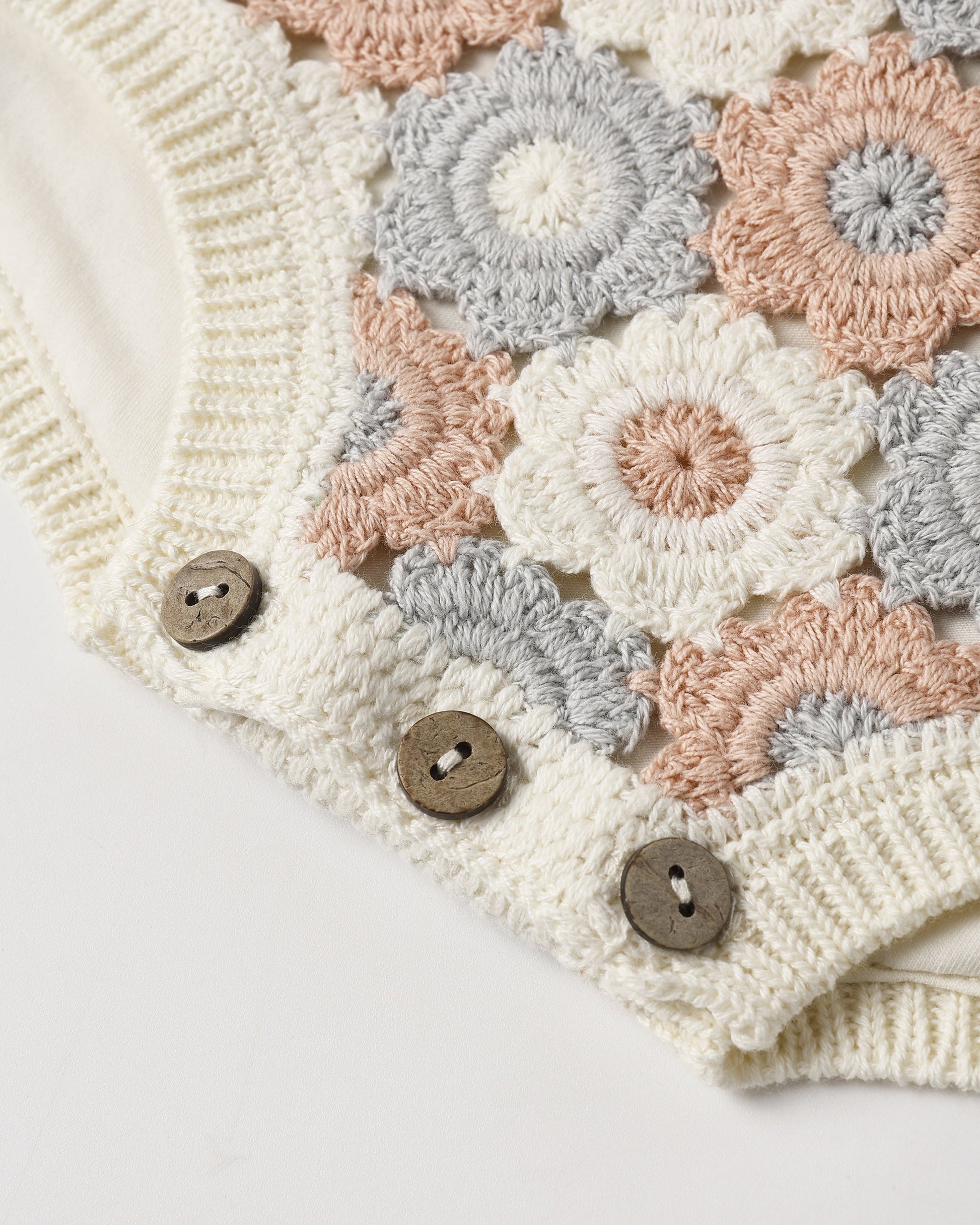 Close-up of the Rylee & Cru Baby Girls' Crochet Romper, featuring a beige, gray, and peach floral crochet pattern, three wooden buttons, and ribbed trim for a vintage-inspired look.