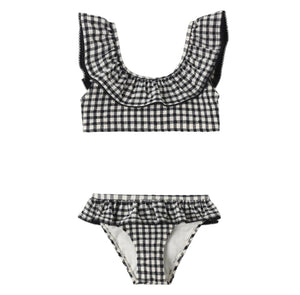 The Rylee & Cru Girls' Margot Bikini features a charming two-piece design in black and white gingham, with a ruffled collar on the top and a matching ruffled waistband on the bottom. This stylish swimsuit also provides UPF 50+ protection, making it perfect for sunny days by the water.