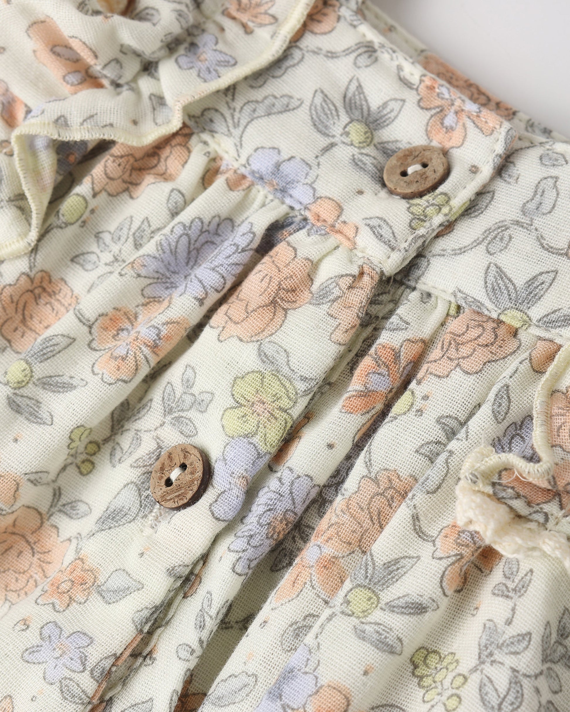 Close-up of the Rylee & Cru Baby Girls' Maya Romper: pastel floral fabric with pleats and round wooden buttons—perfect for a vintage summer look.
