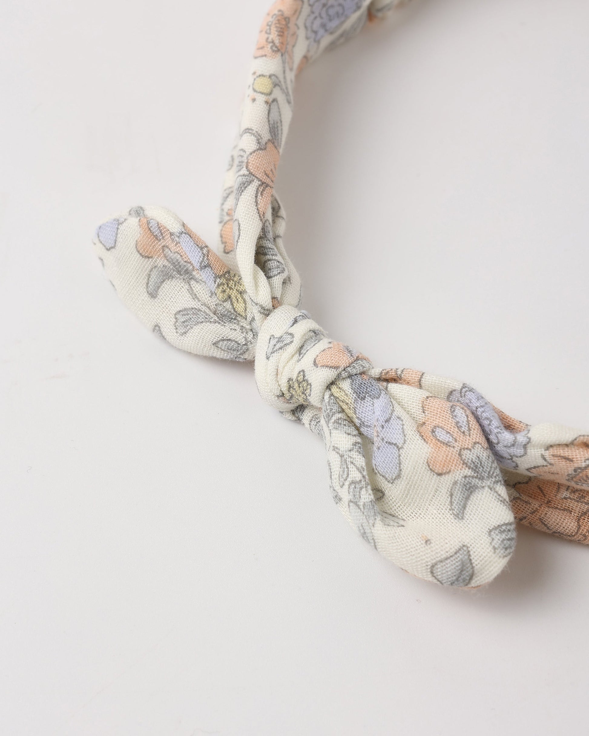 A close-up of the Rylee & Cru Baby Bow Headband, featuring a floral pattern, knotted design, and a scrunchy elastic band, shown against a plain white background.