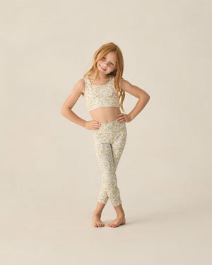 A young girl with long red hair stands barefoot, wearing a Rylee & Cru Girls' Swift Sports Top and matching leggings with a floral print, posing against a plain light background.