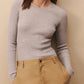 A person wearing the TWP Knit Wool Crewneck in a light gray, vertically ribbed design and khaki pants stands with their hands in their pockets, against a neutral background.