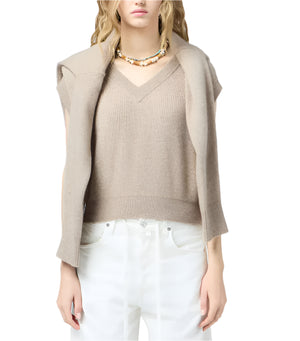 A woman wears the Guest in Residence Rib Vest in beige with a matching cashmere sweater over her shoulders, white pants, and a beaded necklace.