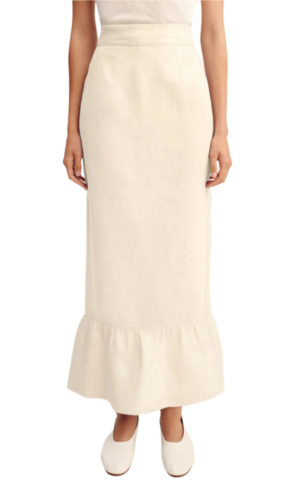 A person wears the POSSE Matilda Column Skirt—a premium linen, high-waisted skirt with a ruffled hem—paired with a white top and white shoes.