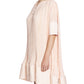 A woman is shown from the side against a white background, wearing the Lanvin Short Sleeve Cascade Dress—a loose-fitting, pleated light pink dress with wide cuffs and a round neckline crafted from soft Korean satin.