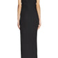 A woman faces away, dressed in the Lanvin Asymmetrical Long Pleated Dress—an elegant, short-sleeved, ankle-length black dress with a draped waist—paired with black open-back heels accented in gold.