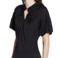 A woman wears the Lanvin Summer Top with Eyelet Detail—a black viscose jersey short-sleeve top featuring pleated sleeves and a metallic-accented keyhole neckline.
