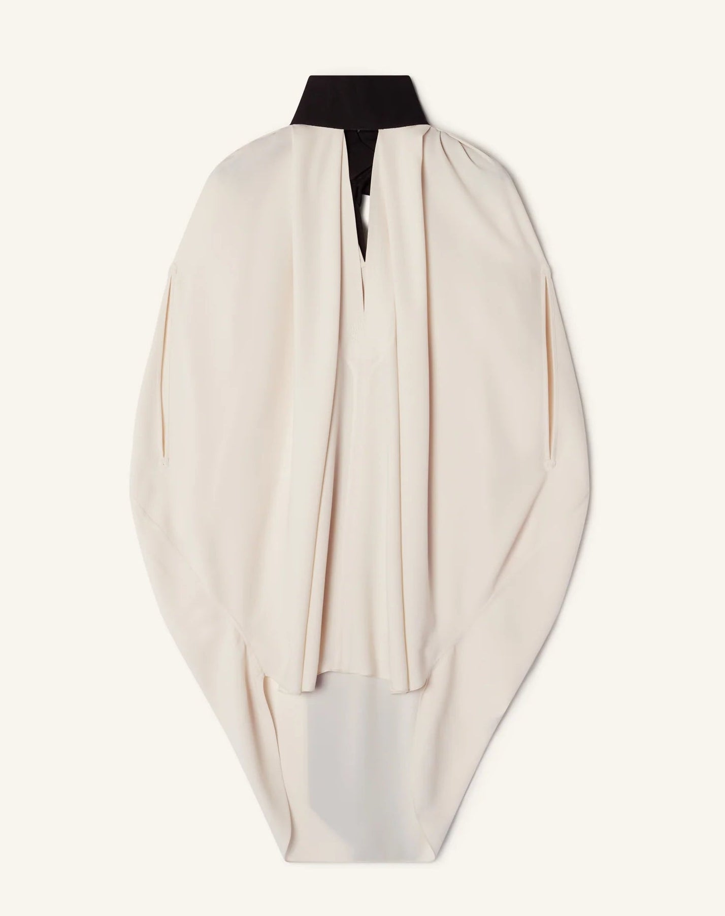 The Lanvin Knotted High Neck Cape is a cream-colored, haute couture, loose-fitting cape with a black stand collar, grosgrain bow detail, and draped sleeves, displayed against a plain light background.