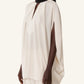 A person wears the Lanvin Knotted High Neck Cape—a loose, off-white cape-style top with slit sleeves and a black grosgrain bow at the neck—paired with matching shorts for a chic Haute Couture look.