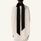A person stands with their back to the camera, wearing Lanvin’s Knotted High Neck Cape in white, featuring a dramatic grosgrain bow at the neck.