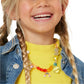 A smiling child with blonde braids wears a yellow shirt, denim jacket, and a colorful chunky necklace made with vibrant beads from the Super Smalls Make It Rainbow Mini Bead Kit.