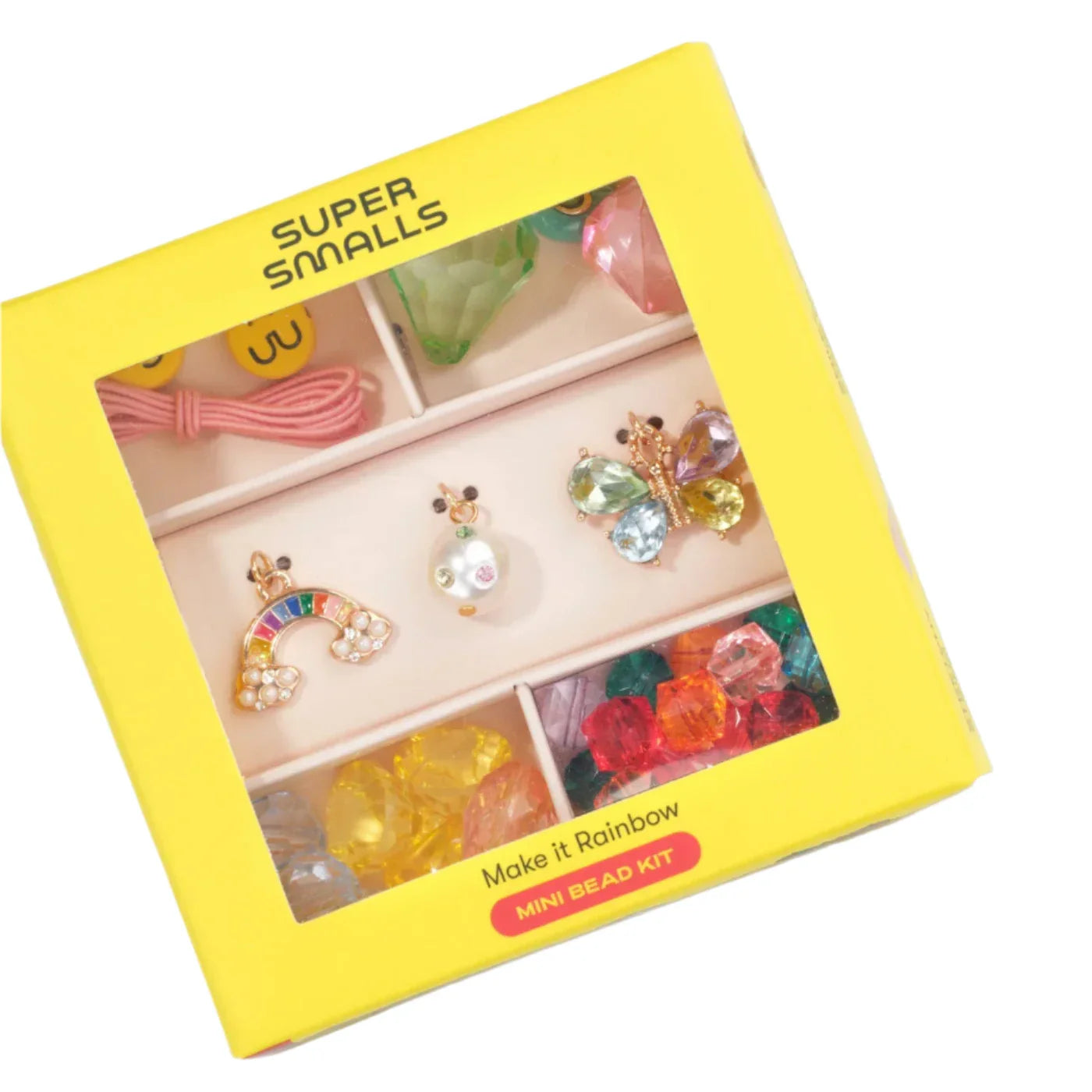 A yellow Super Smalls box holds the Make It Rainbow Mini Bead Kit, with vibrant beads, a pink string, and playful rainbow, butterfly, and pearl charms.