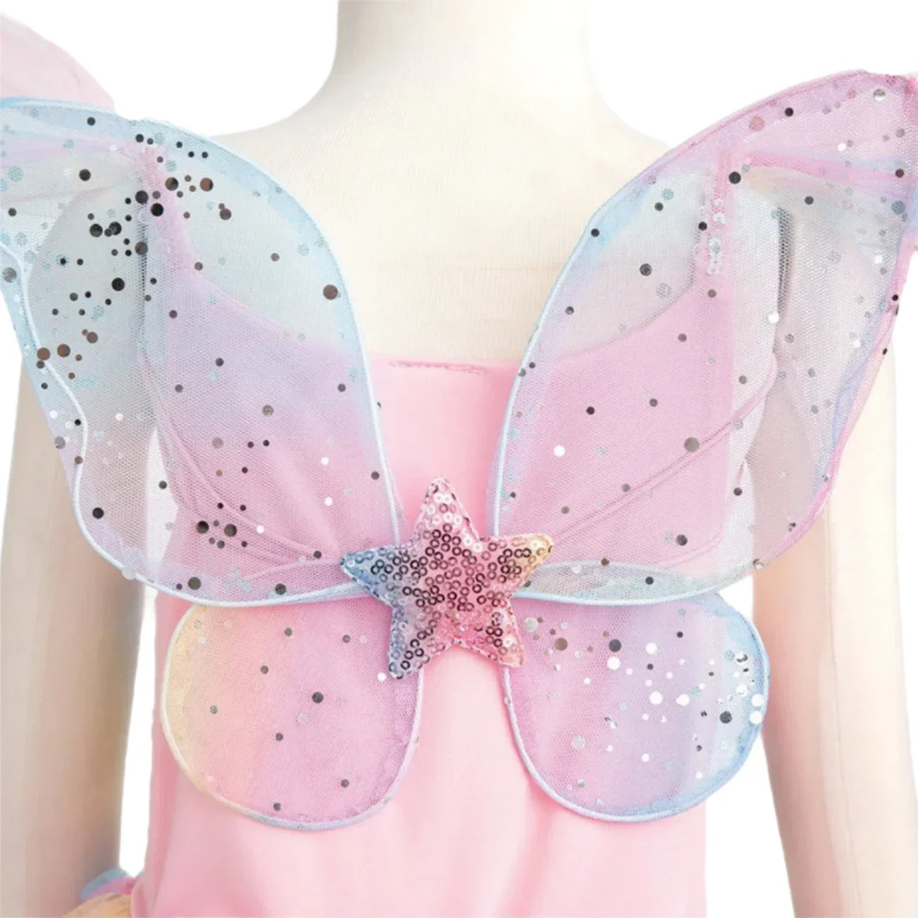 A child twirls in the Great Pretenders Rainbow Fairy Dress & Wings, where the pink fabric is beautifully accented by large, iridescent mesh butterfly wings featuring silver dots and a central sequin star made from shimmery organza.