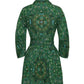 The Raya Mini Dress by Cara Cara showcases a green long-sleeve silhouette adorned with a mandala and paisley print, seen from the back. It features a fitted waist with an elegant sash accent and a flared skirt.