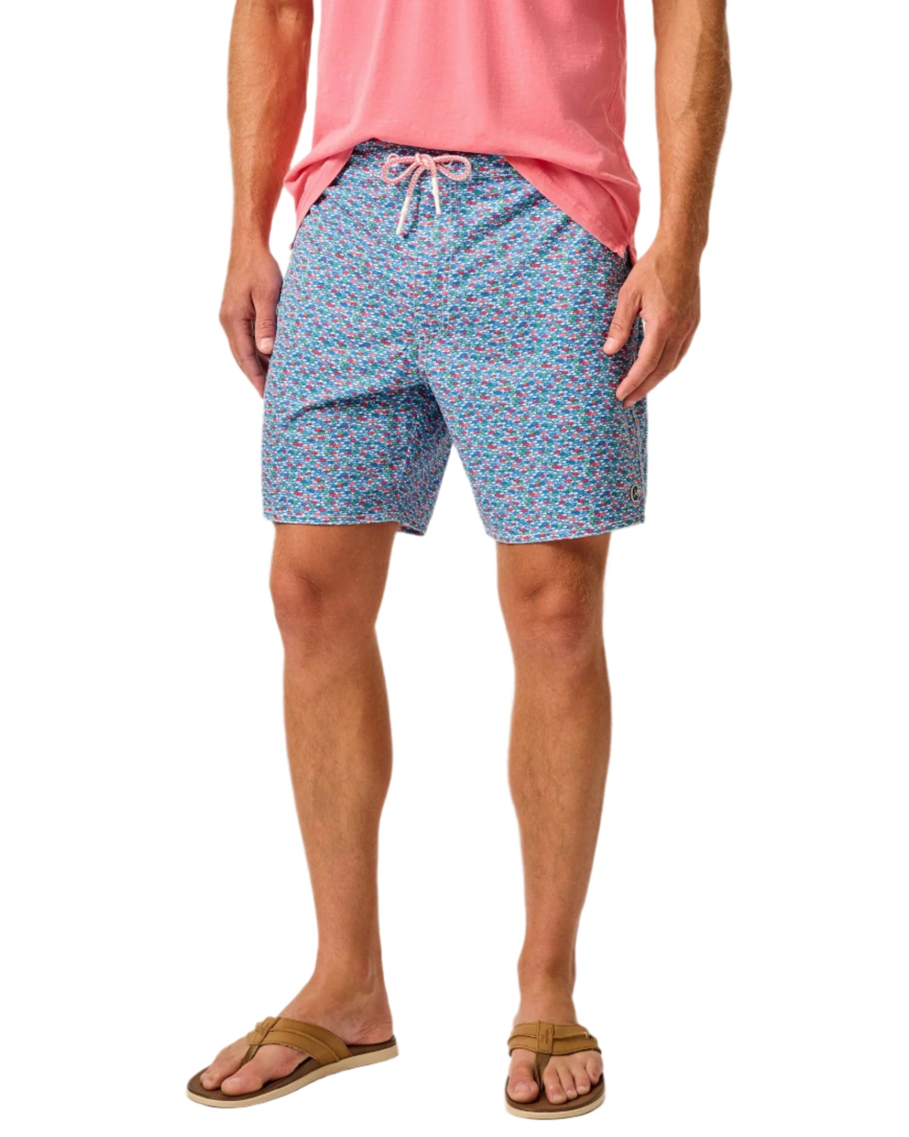 A person wearing a pink shirt, Johnnie-O Red Fin Blue Fin Swim Shorts featuring fun prints, and brown sandals.