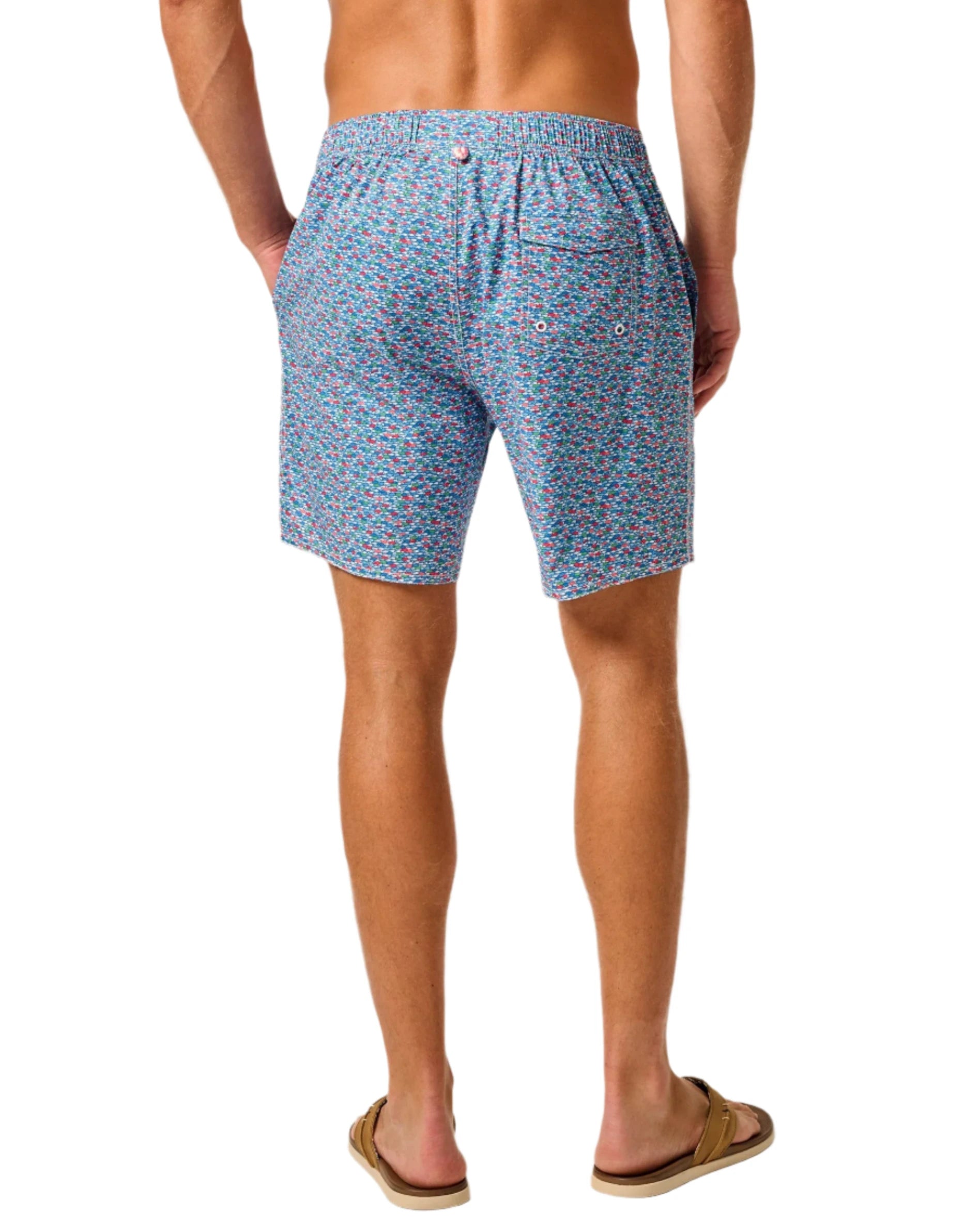 A person wearing Johnnie-O's Red Fin Blue Fin Swim Shorts and brown flip-flops is standing with their back facing the camera.