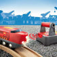 A BRIO World Remote Control Engine toy train by Brio glides smoothly on wooden tracks, set against a backdrop of crane and industrial structure silhouettes.