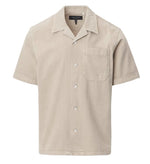 The Rag & Bone Resort Denim Shirt is a beige, short-sleeve camp shirt with a chest pocket, collar, and white buttons, crafted from featherweight denim and shown against a plain white background.