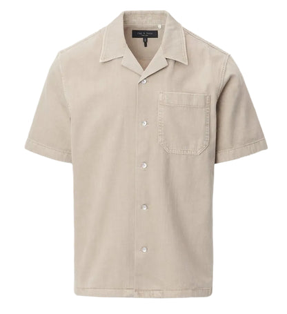 The Rag & Bone Resort Denim Shirt is a beige, short-sleeve camp shirt with a chest pocket, collar, and white buttons, crafted from featherweight denim and shown against a plain white background.