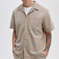 A person in a Rag & Bone Resort Denim Shirt over a white tee, paired with beige pants and showcasing arm tattoos, exemplifies effortless resort style.