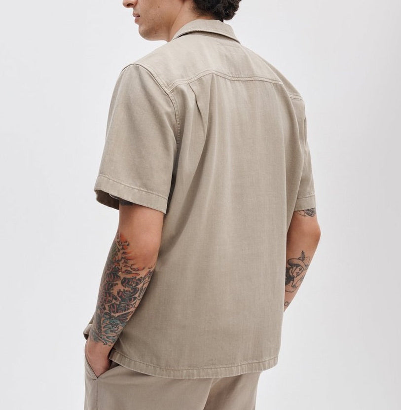 A person is seen from the back wearing the Rag & Bone Resort Denim Shirt with matching pants, hands in pockets and forearm tattoos visible—an effortless look for resort style.