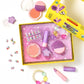 A yellow box contains the Super Smalls Rainbow Gems Beauty Play Kit, which includes kid-safe makeup for pretend play, toy brushes, pretend lipstick, colorful beads, rings, and stick-on nails, all set against a purple star-patterned background.