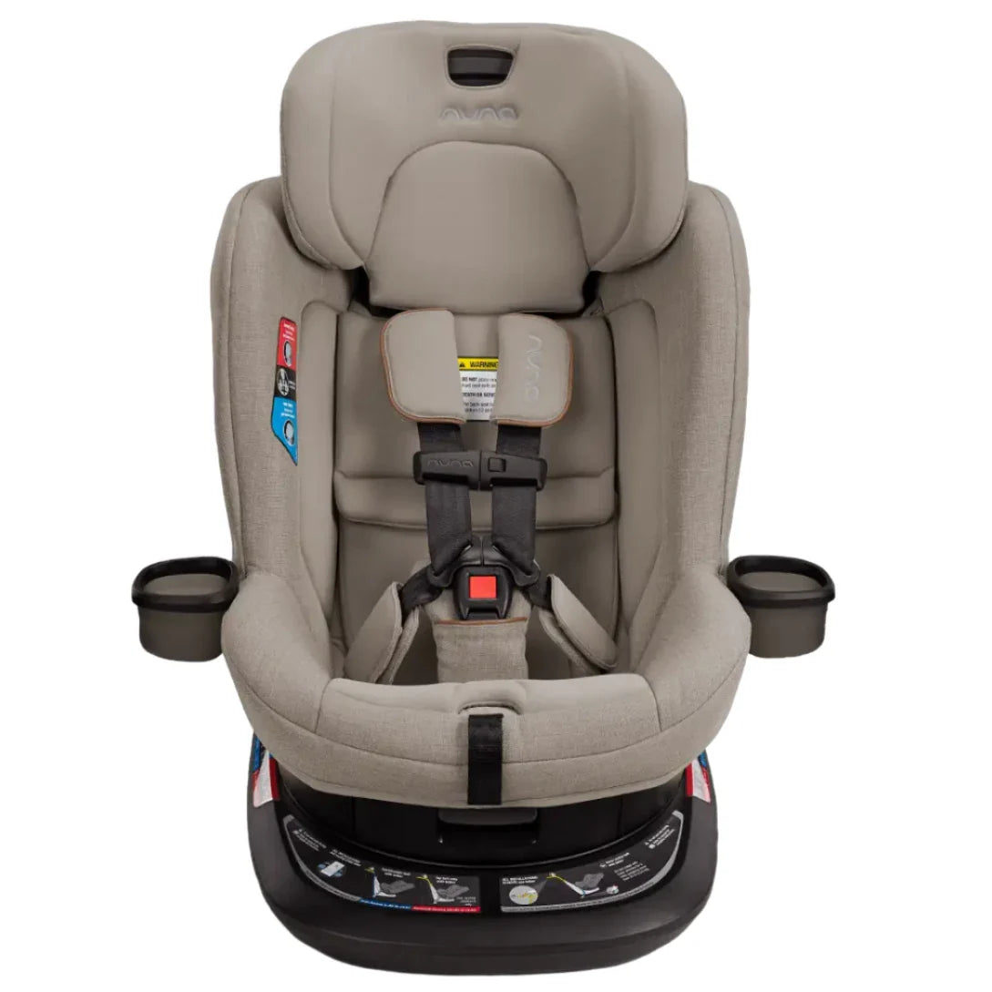 The Nuna Revv Carseat by Nuna is a beige rotating convertible car seat featuring a five-point harness, cup holders on either side, side impact protection, and a black base.