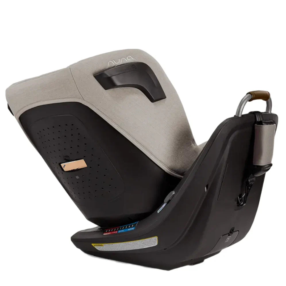 The Nuna Revv Carseat by Nuna is a rear-facing child's car seat in beige and black, featuring a handle, mounted on a black base with safety labels and instruction hints. This rotating convertible car seat easily transitions from rear to forward-facing for growing children.