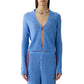 A person wears the Rib Stealth Cardigan by Guest in Residence in blue, partially unbuttoned, with matching ribbed pants and a chunky necklace.
