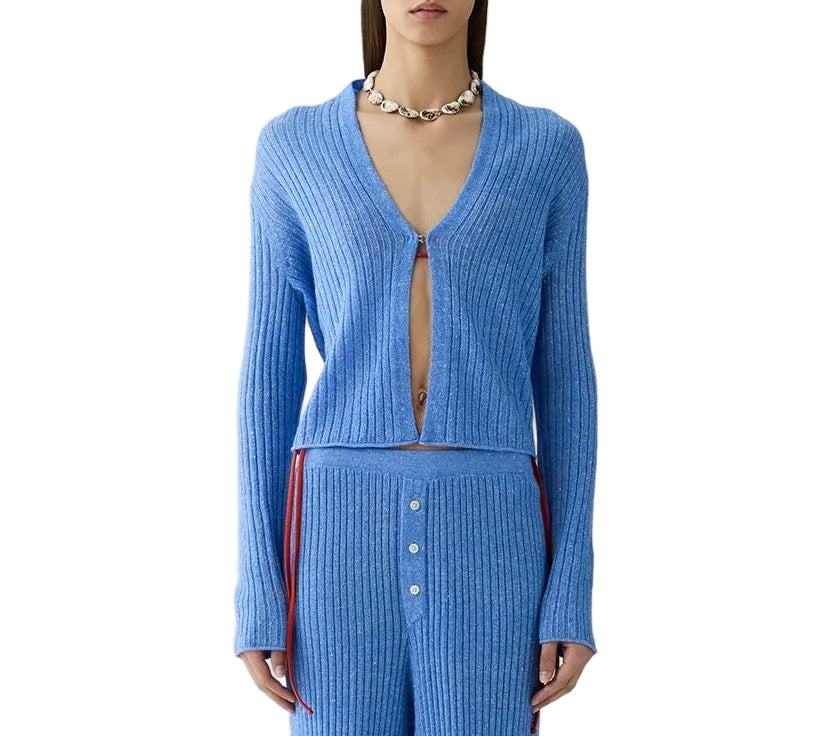 A person wears the Rib Stealth Cardigan by Guest in Residence in blue, partially unbuttoned, with matching ribbed pants and a chunky necklace.