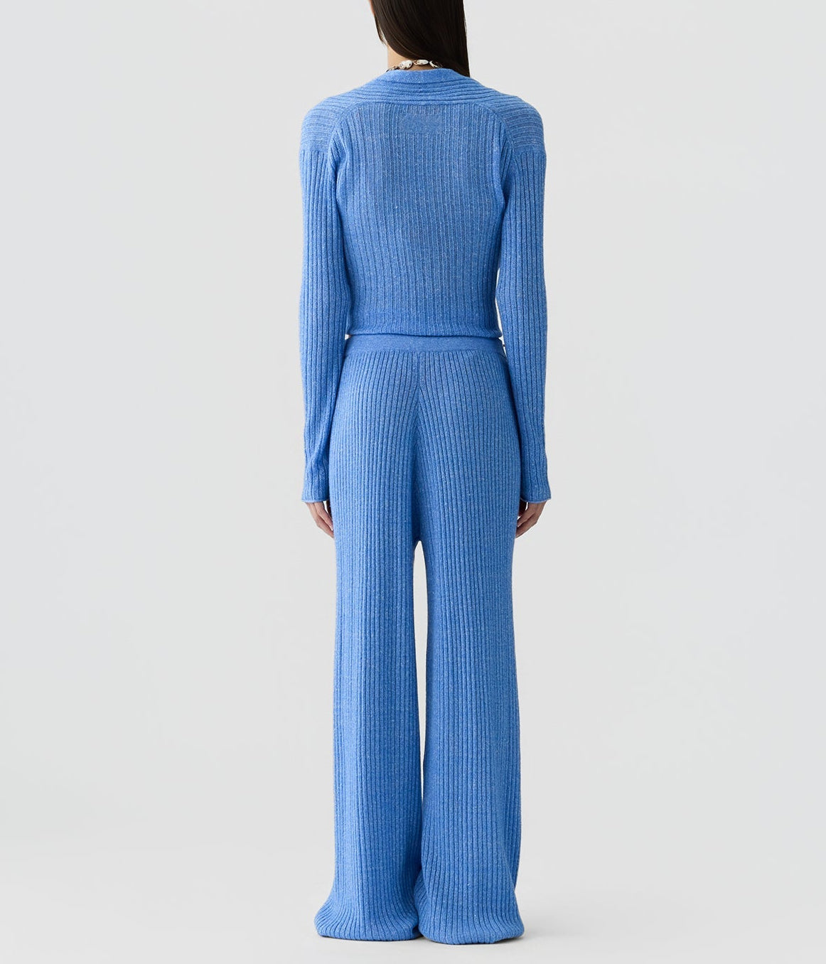 A person stands facing away in a matching blue ribbed knit long-sleeve top and Rib Everywear Pant by Guest in Residence, featuring wide legs, against a plain light background.