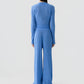 A person stands against a plain background, shown from the back, wearing Guest in Residence’s Rib Stealth Cardigan layered over a matching blue ribbed knit long-sleeve top and wide-leg pants.