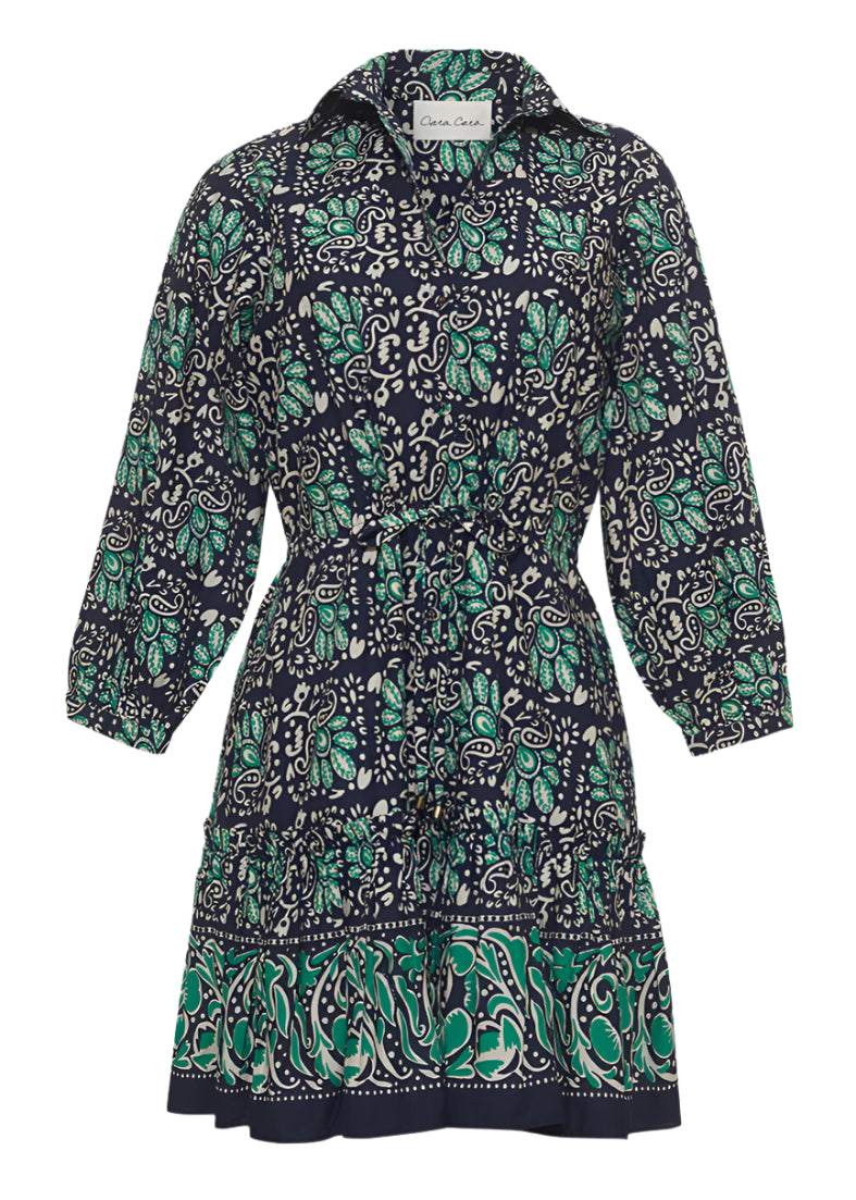 The Cara Cara Robin Dress is a knee-length piece adorned with a navy, green, and white paisley pattern. It boasts a collared neckline and gathered waist, accented by a subtle ruffle tier skirt for extra elegance.