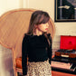 A young girl stands indoors wearing the Louis Louise Girls' Alinou Wool Blend Pull, paired with a leopard print skirt; a wicker chair and a red record player are in the background.