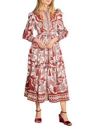 A woman wears the Rosie Dress by Hunter Bell NYC, a long-sleeved, mid-length holiday dress with a red and white Central Park Toile pattern, paired perfectly with red open-toe heels.