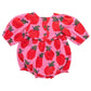 The Pink Chicken Baby Girls' Rowan Bubble is a pink infant romper adorned with a pattern of large red graphic apples and green leaves. This charming garment features glitter buttons on the back and gathered cuffs at the sleeves and legs.