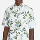 A person wearing the Rubie Dress by Emilia Wickstead, a white cotton dress with short sleeves featuring a green and blue floral print, shown from the shoulders to the waist.
