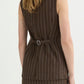 A woman is seen from behind wearing the POSSE Emma Pinstripe Vest, a brown sleeveless vest with a belt detail and matching skirt, creating a timeless silhouette.