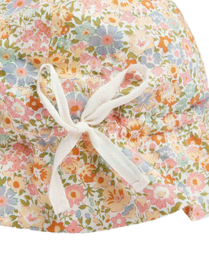 Close-up of Bonpoint's Grigri Hat with Ties for babies, made from soft Liberty fabric and adorned with multicolored flowers and a white bow at the center.