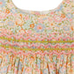 Close-up of the Bonpoint Baby Girls' and Girls' Maruska Smocked Dress made with Liberty fabric, featuring pastel floral patterns and detailed pink and green hand-embroidered smocking across the chest.
