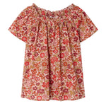 The Bonpoint Girls' Goldia blouse in Liberty Fabric features short sleeves, a pink, red, and orange floral pattern, soft organic cotton material, and a gathered elasticated neckline.