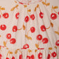Close-up of Bonpoint's Girls' Leontine Dress with Ruffles, featuring a cream-colored organic cotton fabric adorned with vibrant red and yellow cherry prints and a gathered neckline.
